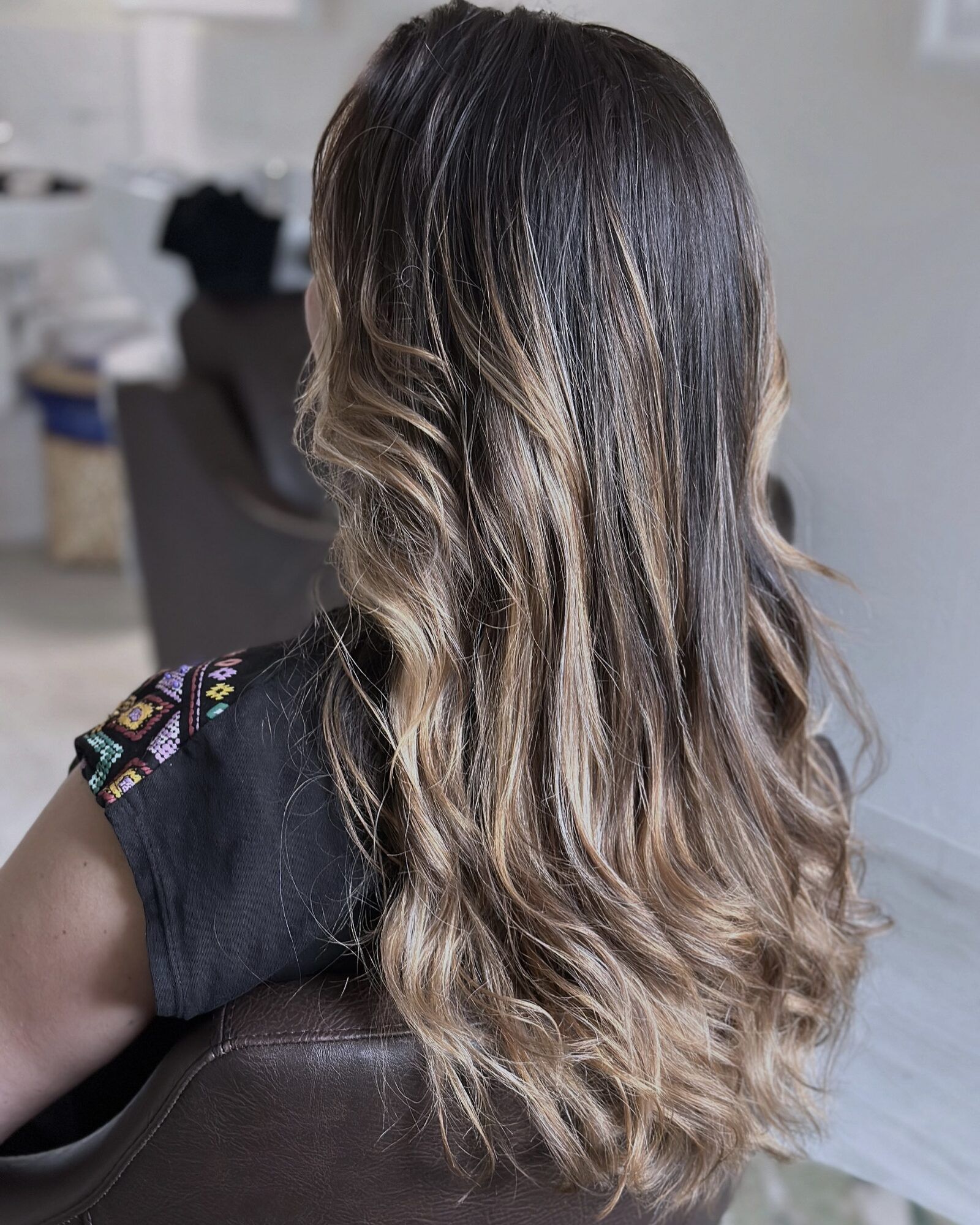 Dunkelbraunes Haar mit blonden Balayage-Strähnen, das in weichen Wellen über den Rücken fällt