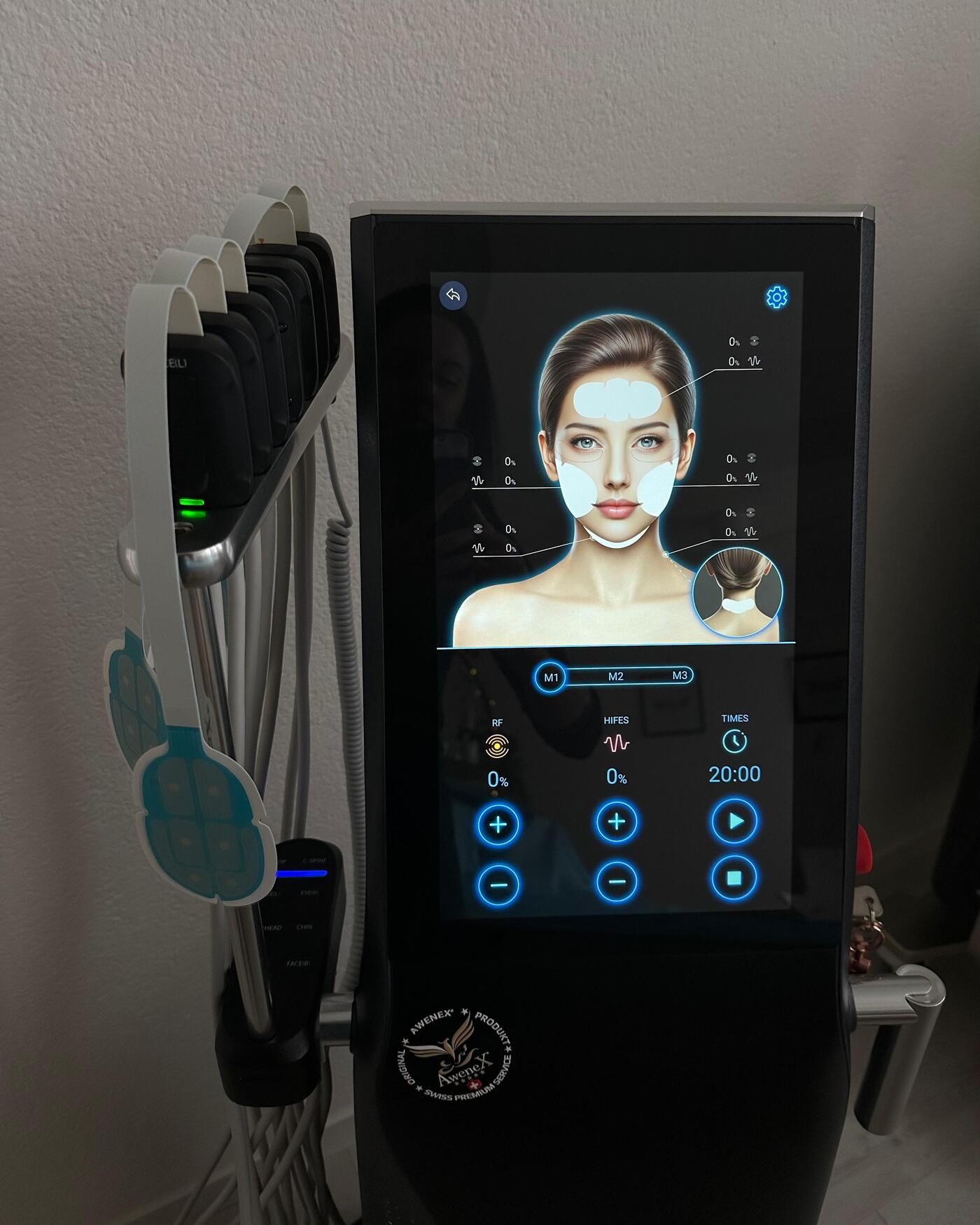 Touchscreen des EMVisioX-Geräts mit Gesichtsdiagramm und Behandlungszonen, daneben hängende Gesichts-Pads