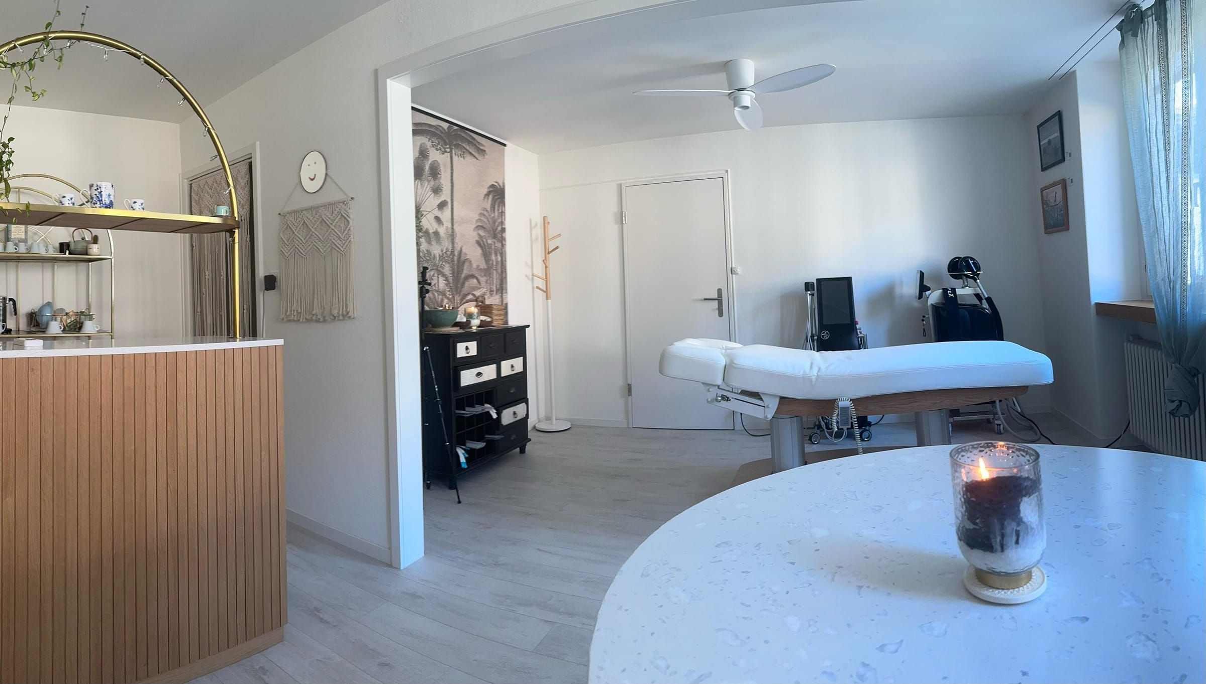 Heller Behandlungsraum im Canelas Natural Beauty Center mit weisser Liege, Palmen-Wandbild und rundem Steintisch